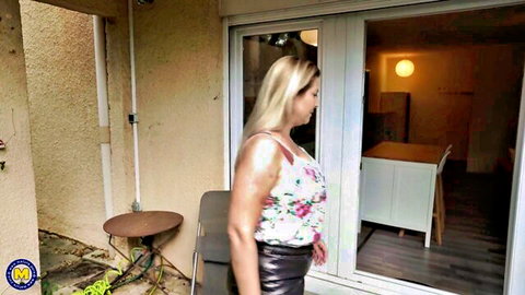 Blonde babe in sheer floral tank top showing sideboob and tight leather pants by patio door