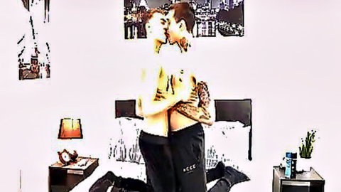 Two shirtless tattooed young gay hunks passionately kissing and embracing in bedroom