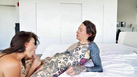 Skinny tattooed brunette babe with medium tits passionately kissing tattooed man's thigh near cock on bed