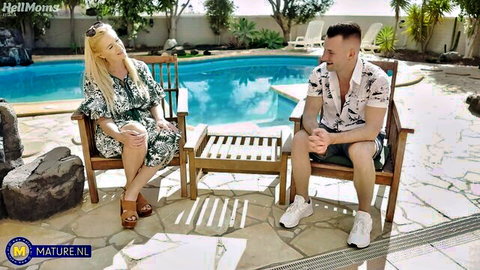 Mature blonde woman in dress flirts with nephew by pool