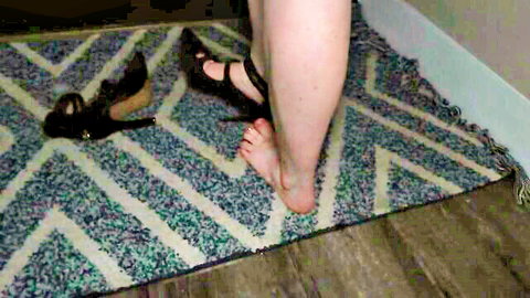 Delilah Cass in black strappy heels, bare foot with red toes, foot tease