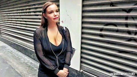 Busty Latina in sheer black top with deep cleavage, posing against graffiti wall