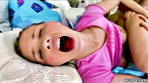 Blonde teen yawning wide in pink top and diaper on bed
