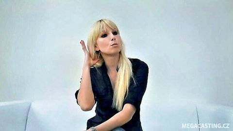 Blonde teen in black top gestures seductively on casting couch showing cleavage