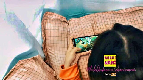 Sharinami lying on bed in orange top, playing Mobile Legends on phone