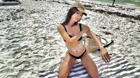 Lucy Mochi in black bikini on beach, seductive spread-leg pose