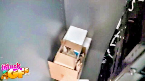 Cluttered gray storage closet with stacked cardboard boxes and hanging black clothes rack