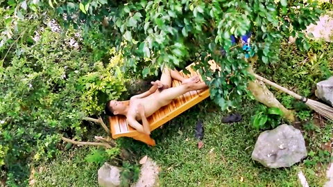 Young East Asian guy naked on outdoor lounge chair stroking his erect cock in lush garden.