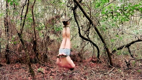 Naked man upside down in forest shibari suspension bondage with legs spread and exposed cock