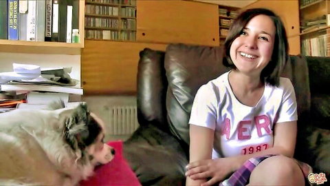 Cute smiling teen girl in white tee and purple skirt sits happily with fluffy dog on leather couch