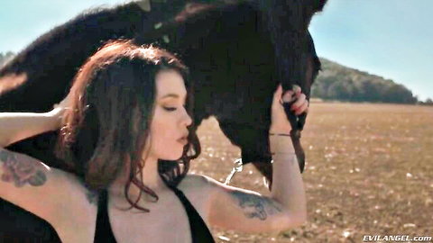Tattooed redhead in tank top poses intimately with black horse outdoors, small tits tease