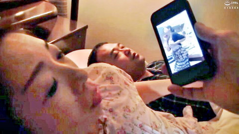 Asian MILF puckers plump lips toward sleeping husband's crotch for sneaky blowjob while he holds phone