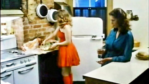 Blonde Juliet in orange mini dress and stockings washes dishes with brunette in kitchen