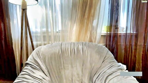 Empty white armchair in luxurious bedroom with beige curtains and tripod lamp