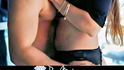 Muscular tanned stud hugs busty blonde babe from behind in tight black outfit on balcony