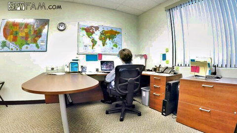 Blonde woman in white blouse sitting at office desk with maps on wall