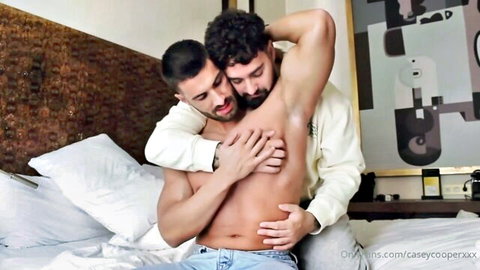 Muscular gay men passionately embracing on bed groping shirtless hunk's ripped torso