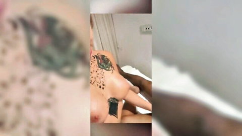 Blurry tattooed woman exposing tits and tattoos lying nude on bed with dark skin nearby