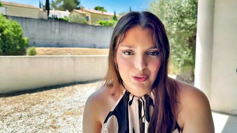 Brunette woman with fair skin smiling seductively in revealing black and white halter dress outdoors showing cleavage