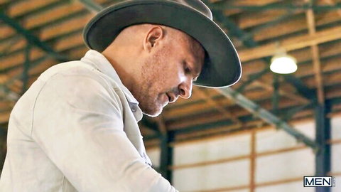 Handsome bald bearded man in green fedora hat looking pensive in barn warehouse gay teaser