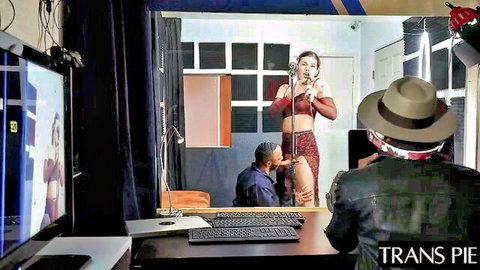 Trans woman in red sparkling dress performs on stage with men watching