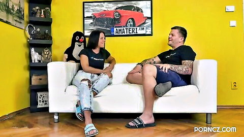 Moly 30 in black top and jeans with tattooed guy on sofa