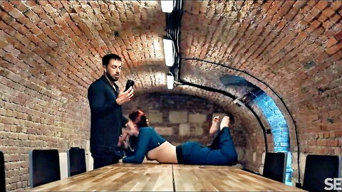 Mia Evans topless redhead seducing suited man on table in blue pants