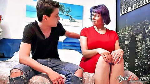 Mature purple-haired granny in red dress chats intimately with young guy on bed