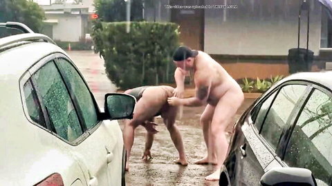 Naked muscular man fists woman's spread pussy outdoors in rain next to cars