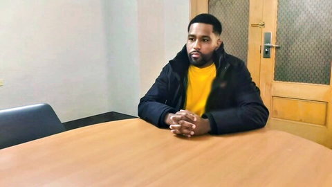Handsome black man with beard sits pensively at office table in yellow shirt and black jacket