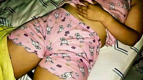 Slim Asian girl in cute pink bunny pajamas lifting top to tease stomach