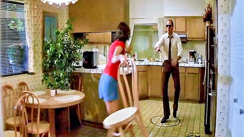 Brunette in red top and blue shorts startled by suited man in Poltergeist parody
