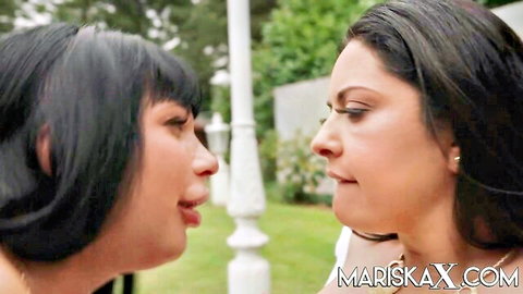 Two sexy Asian women in close seductive foreplay stare intensely lips parted outdoors