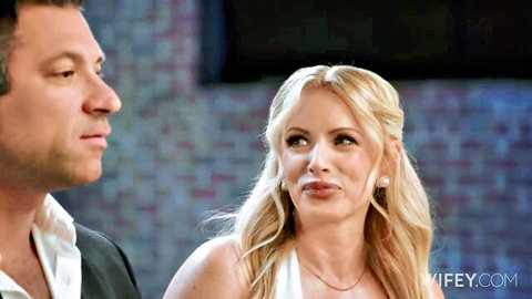 Blonde wife in white dress seductively eyes suited man in intimate closeup
