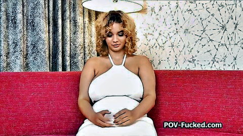 Curvy blonde with massive natural tits in low-cut white halter dress teasing deep cleavage on red sofa