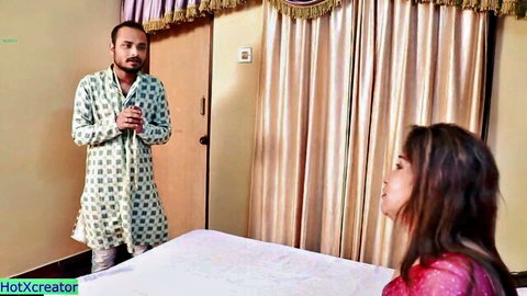Indian Bhabhi in red saree sits seductively as man in green kurta stands nearby, Desi tease scene
