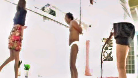 Japanese femdom scene with two women whipping submissive man in briefs