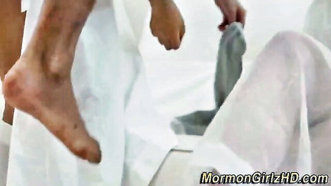 Mormon teen brunette raises bare leg in white temple garments as hands pull down gray panties on bed