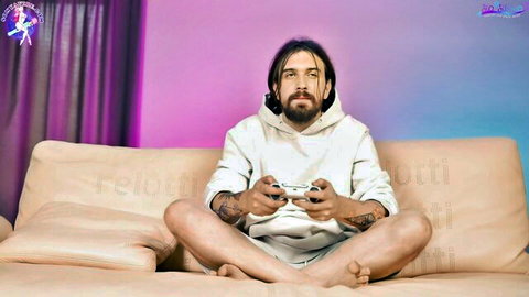 Brunette gamer guy with long hair and beard holding Xbox controller on couch in white hoodie and shorts