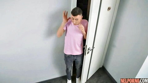 Young man in pink shirt peeking surprised from behind white bedroom door