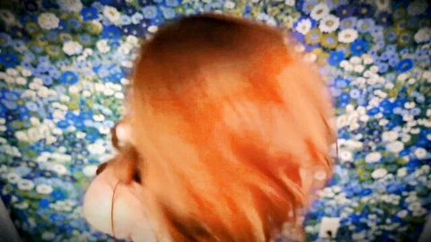 Blurry close-up of redhead's tousled hair and profile from behind against blue floral wallpaper