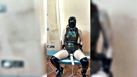 Latex-clad masked woman tied to chair with dildo penetration in BDSM solo