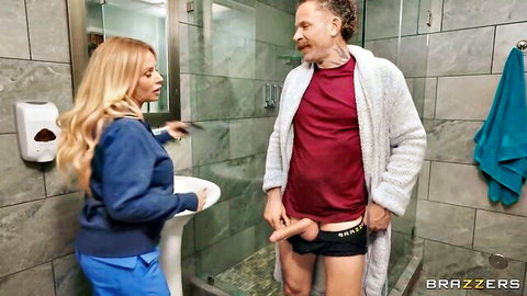 Blonde nurse in blue uniform holding older man's cock in steamy bathroom scene
