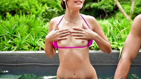 Smiling brunette in pink bikini, topless by pool, man embracing her from behind