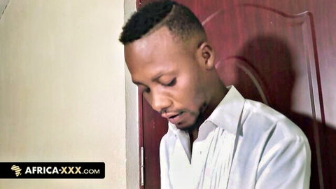 Young ebony man with fade haircut looking down pensively in white shirt by red door