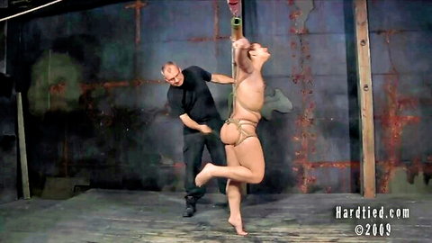 Flexible bound woman suspended in ropes by dominant man for intense vibration play