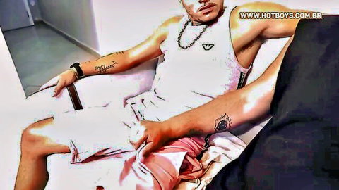 Tattooed muscular hunk pulls aside pink briefs to stroke his massive erect cock on white couch