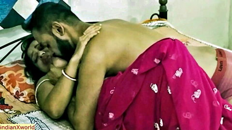 Bearded Indian man passionately kisses busty woman in red saree exposing cleavage on bed