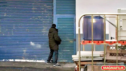 Clothed man in green parka walking toward blue garage door outdoors