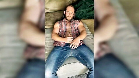 Muscular bearded man lounging in open plaid shirt and jeans